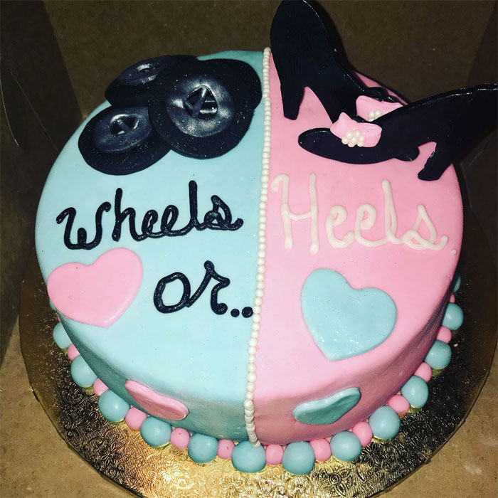 A split gender reveal cake with 'Wheels' in blue and 'Heels' in pink, symbolizing a gender reveal moment.