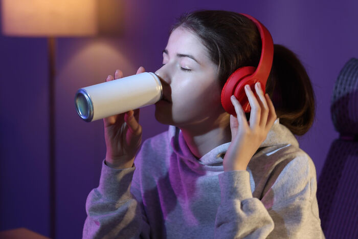 A young woman with red headphones sips from a white can, illustrating common things that may be worse than we realize.