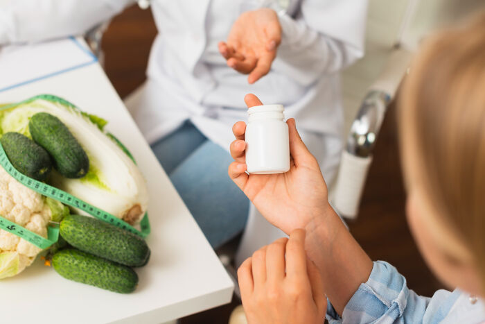 A person holding a pill bottle, with vegetables on a table, highlighting common things that are worse than we realize.