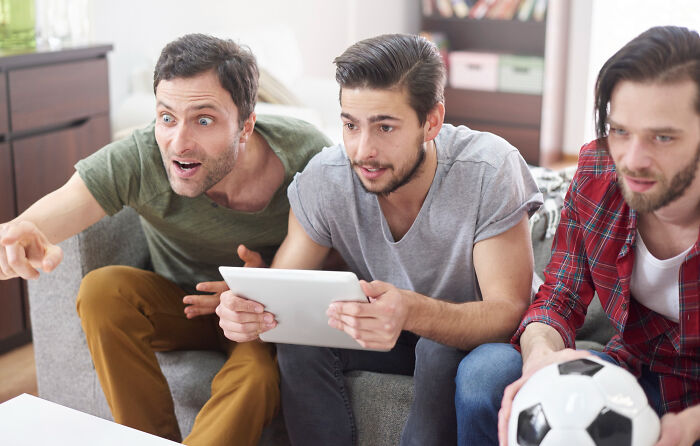 Three men watching a sports game on a tablet, with one pointing enthusiastically, depicting common things worse than we realize.