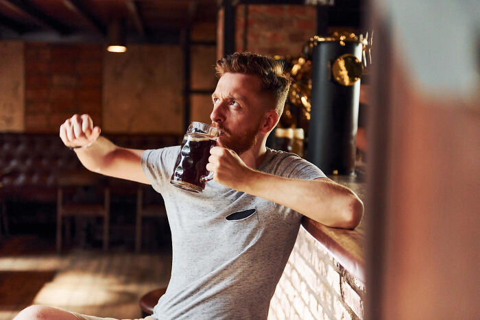 A man with a red beard drinking a dark beer in a dimly lit bar, symbolizing common things that are worse than we realize.