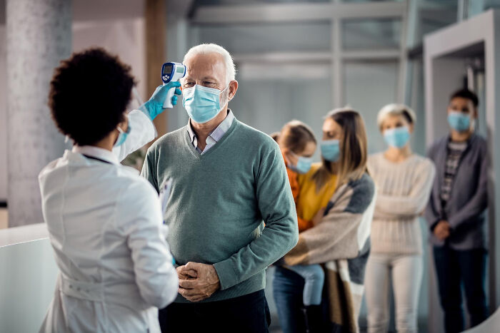 Medical staff checking an elderly man's temperature at a hospital entrance, showing common things worse than we realize.