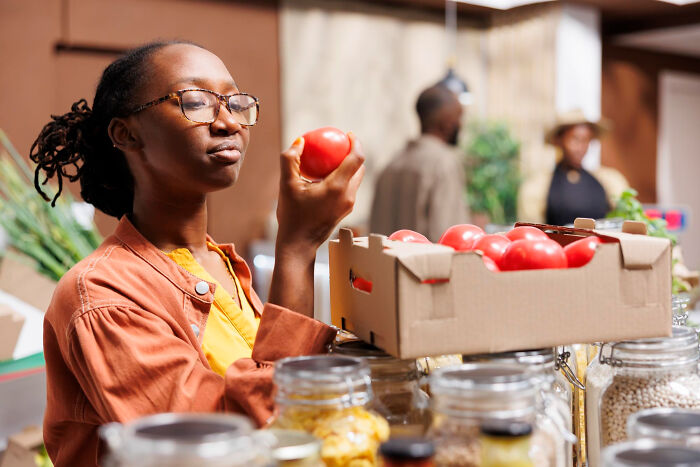 A woman examining a tomato in a grocery store, representing common things that may turn out to be worse than we realize.