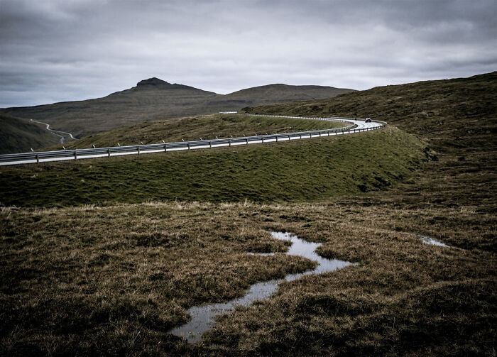 A winding road through a mountainous landscape with a small puddle in the foreground, representing common things.