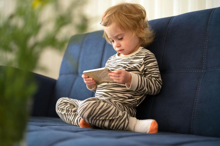 A small child in zebra pajamas sits on a blue couch, engrossed in a tablet, symbolizing common things in daily life.