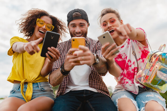 Three friends laughing and pointing at the camera while looking at their phones, representing common things that may be worse than we realize.