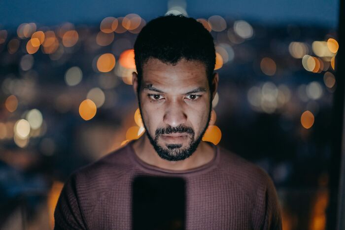 A man with a serious expression looks down, illuminated by a screen, showing subtle signs someone isn't nice.