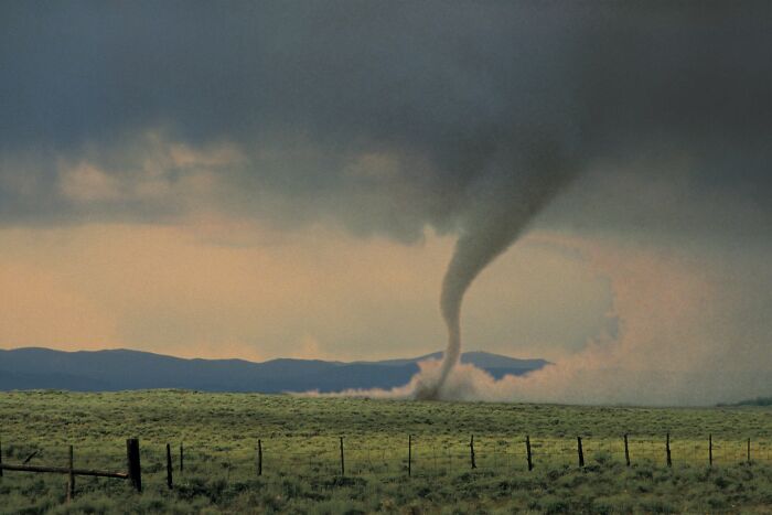 A powerful tornado swirling over a vast green field with distant mountains, depicting scary babysitting stories.