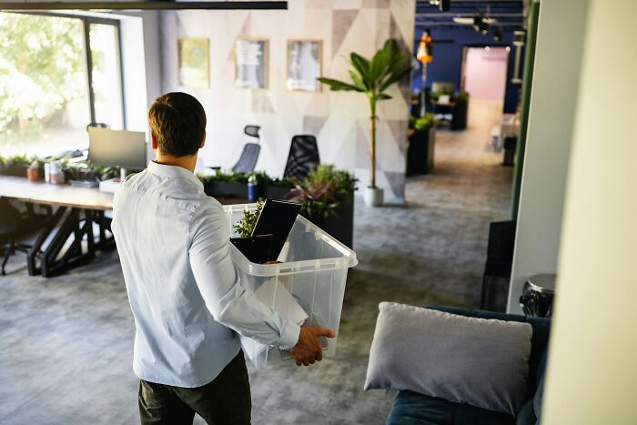 A man carrying a box of personal belongings, leaving an office, evoking a feeling of intuition about change.
