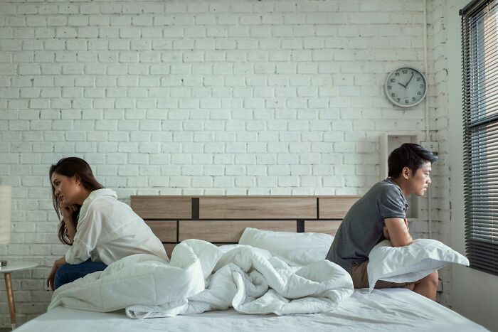 A divorced couple sits on opposite sides of the bed, backs turned, reflecting on their marriage and the moment it was over.