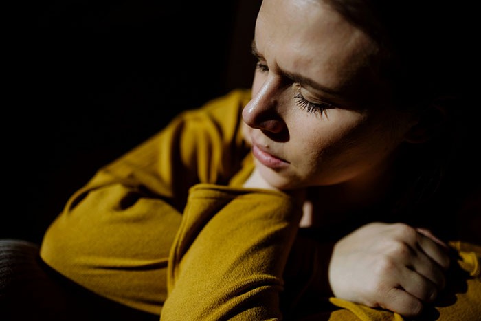 A young woman appears sad and contemplative, lit by a streak of sunlight, reflecting on a cruel prank. A young woman appears sad and contemplative, lit by a streak of sunlight, reflecting on a cruel prank.