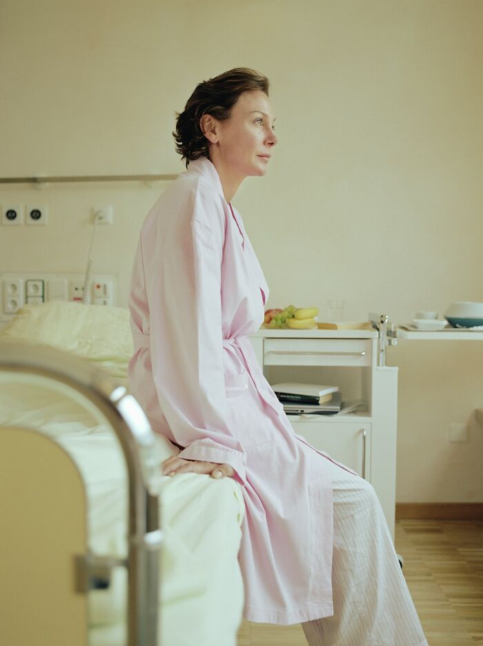 A woman in a hospital gown sits on a bed, contemplating the rarest things that have happened to her.