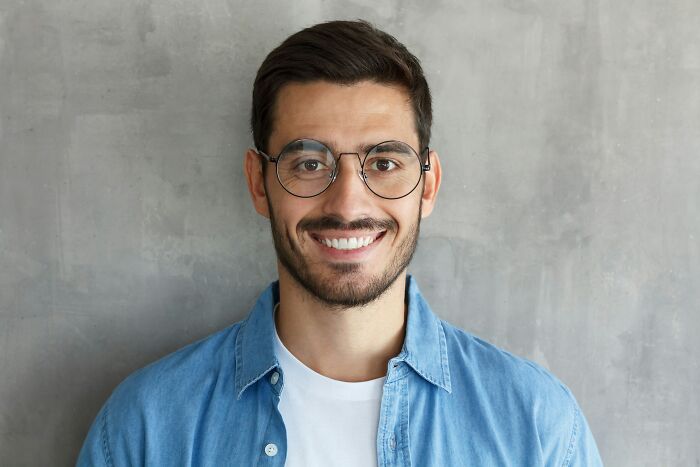 A smiling man wearing glasses, contrasting with subtle signs someone isn't as nice as they pretend to be.