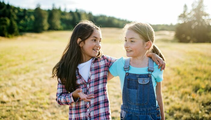 Two young girls smiling together outdoors, showcasing people's intuition.
