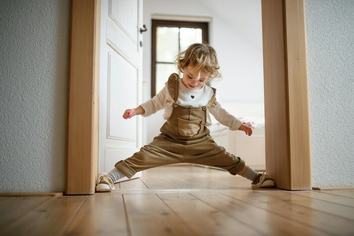 A cheerful toddler playfully stretching in a doorway, embodying delightful babysitting stories.