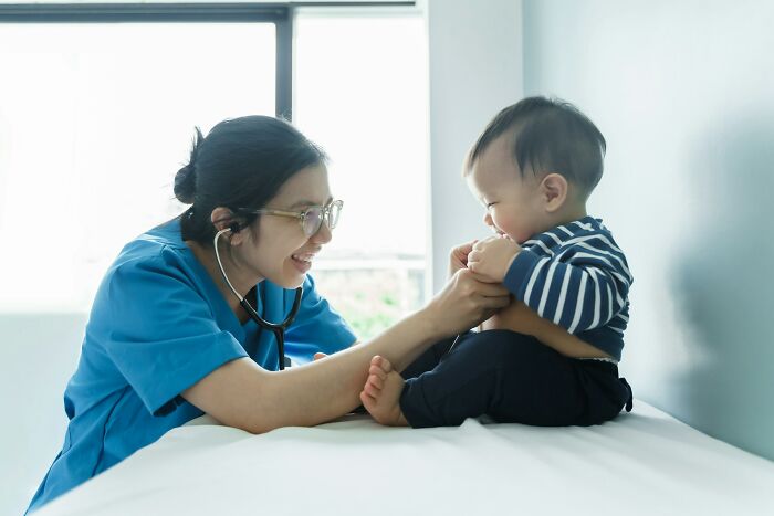 A medical professional with glasses and a stethoscope smiles at a baby during a check-up, showcasing micro feminism.