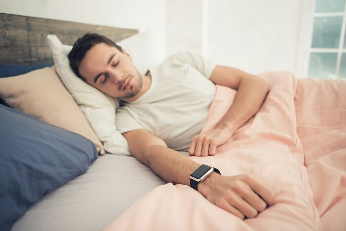 A man sleeps in bed with a smartwatch, a cheating red flag hinting at secret activities.