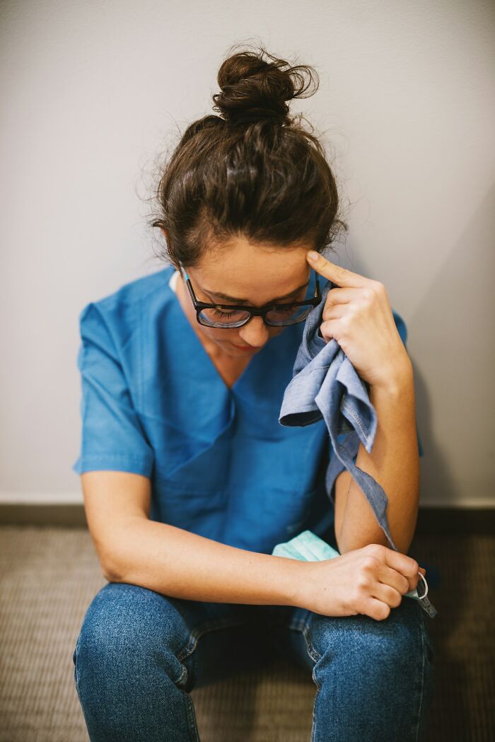 A female medical worker, looking stressed, holds a cloth to her head, emphasizing the impact of medical mistakes.