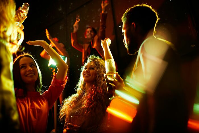 People enjoying a lively party, their intuition guiding them to fun, dancing under colorful lights with drinks in hand.