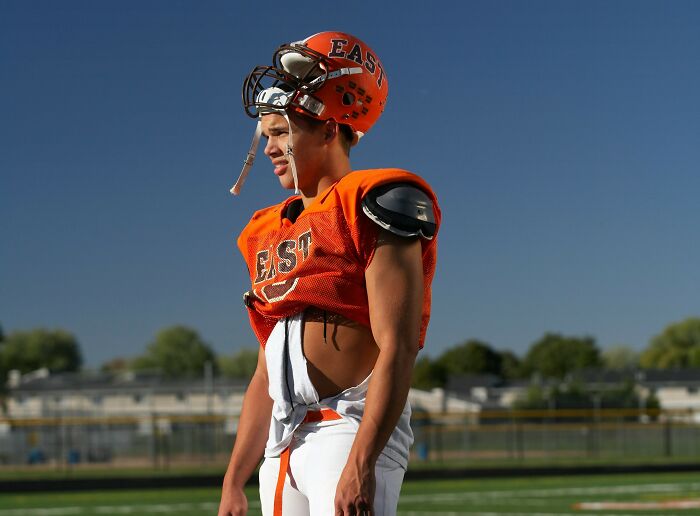 A young football player in an orange uniform on a field, reflecting trends and audience shifts.