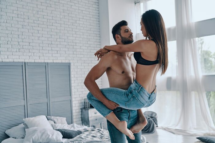 A man holding a woman close in a bedroom, demonstrating the connection in the Queening intimate position. A man holding a woman close in a bedroom, demonstrating the connection in the Queening intimate position.