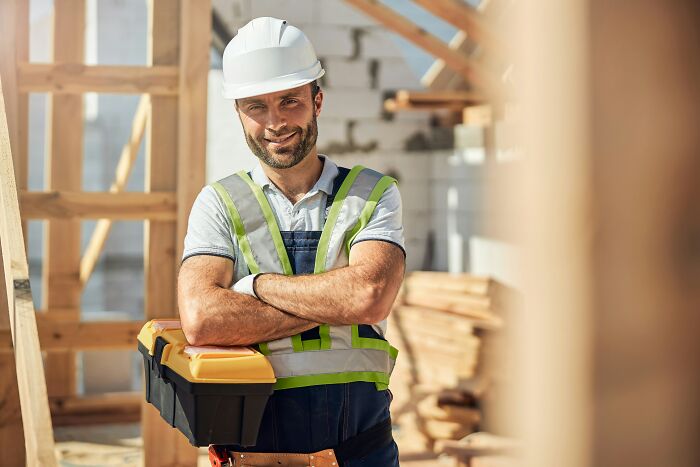A smiling construction worker with a toolbox, demonstrating how people see their jobs.
