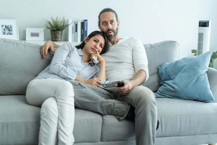 A couple looking terrified while watching TV, experiencing a "we need to leave now" moment.