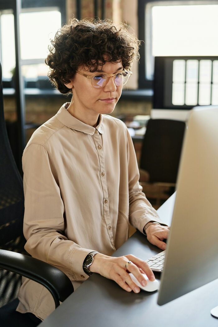 A focused woman with curly hair and glasses works at a computer, representing a common office story.