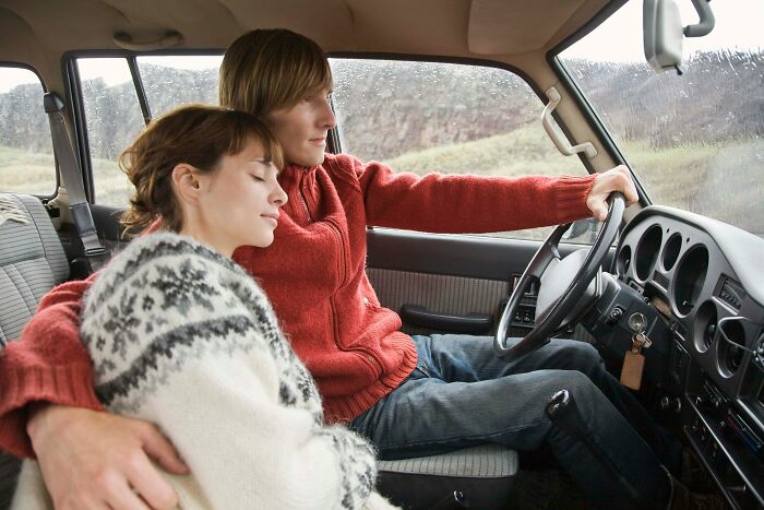 A couple in a car; the man drives, the woman rests on him, perhaps about being cheated on.