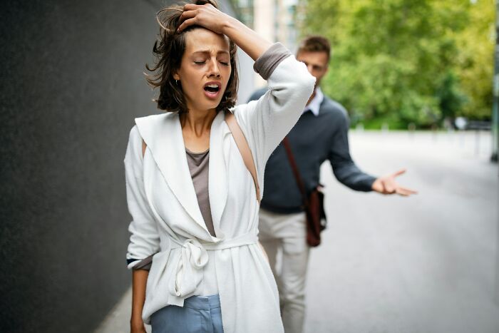 A woman looking distressed with a man in the background, showing painful ways men were made aware they were being cheated on.