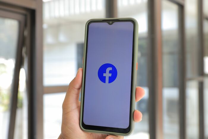 A hand holding a smartphone displaying the Facebook logo, highlighting men being cheated on.