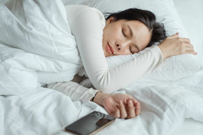 A woman sleeping in bed with a phone nearby, unaware of being cheated on.