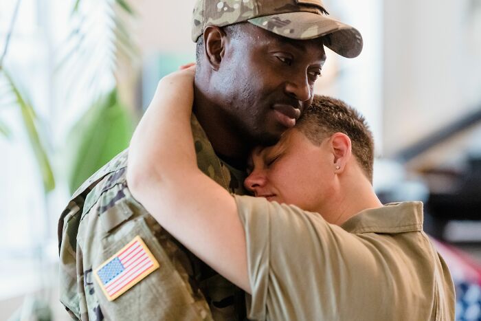 A man in military uniform being embraced by another person, showing emotional pain from being cheated on.