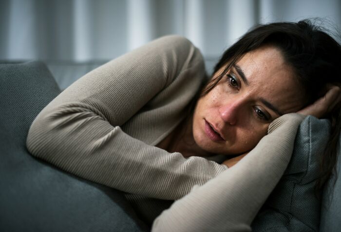 A distressed woman lying on a couch, showing the pain of being cheated on.
