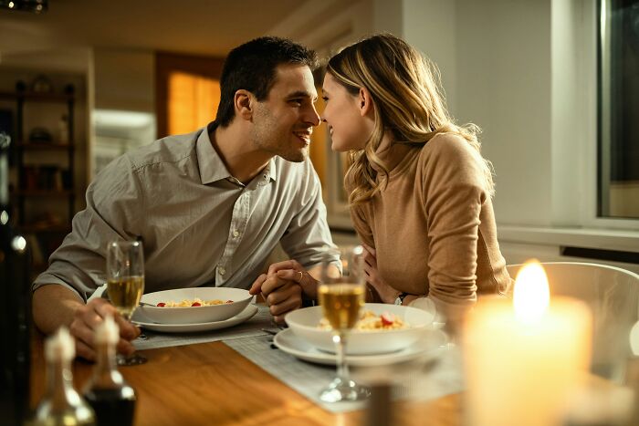A couple looking lovingly at each other over a candlelit dinner, contrasting with being cheated on.