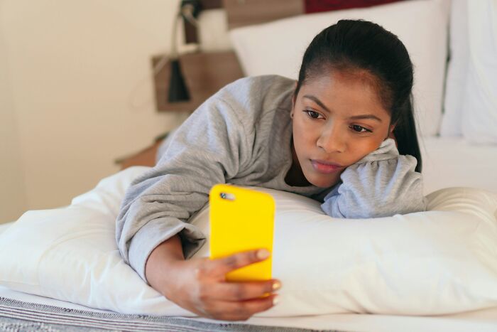 A woman looking sad while using her phone in bed, possibly being cheated on.