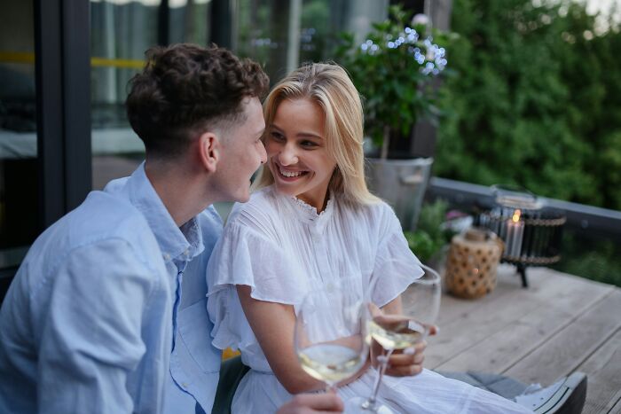 A happy couple on a balcony, smiling and holding wine glasses, contrasting with being cheated on.
