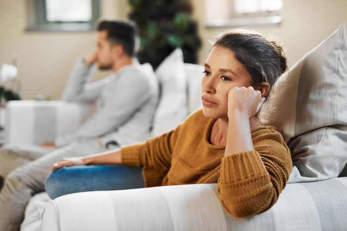 A couple sits apart on a couch, appearing upset, contemplating a groomsman boycotting a wedding due to his toxic GF. A couple sits apart on a couch, appearing upset, contemplating a groomsman boycotting a wedding due to his toxic GF.