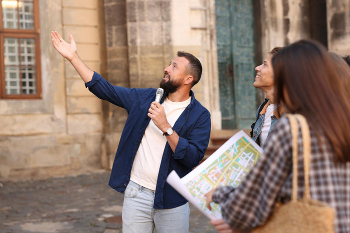 A tour guide starting a tour, speaking into a microphone and gesturing to a group of tourists, unconcerned about late arrivals. A tour guide starting a tour, speaking into a microphone and gesturing to a group of tourists, unconcerned about late arrivals.