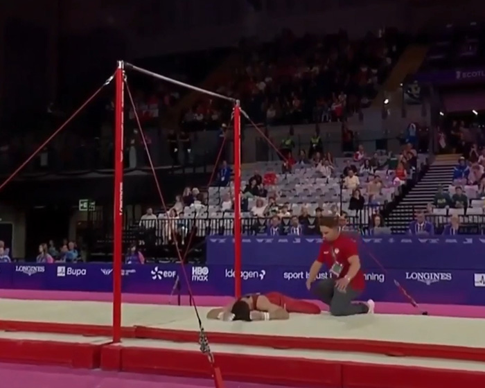 An English gymnast lies on the floor after a horrific fall during the Commonwealth Games, with a medical staff member kneeling beside him.