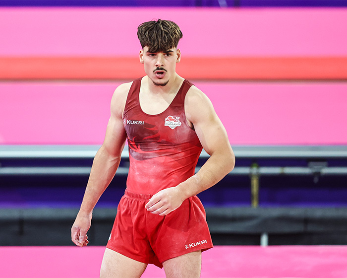 Portrait of an English gymnast in a red uniform, standing on the mat during the Commonwealth Games.