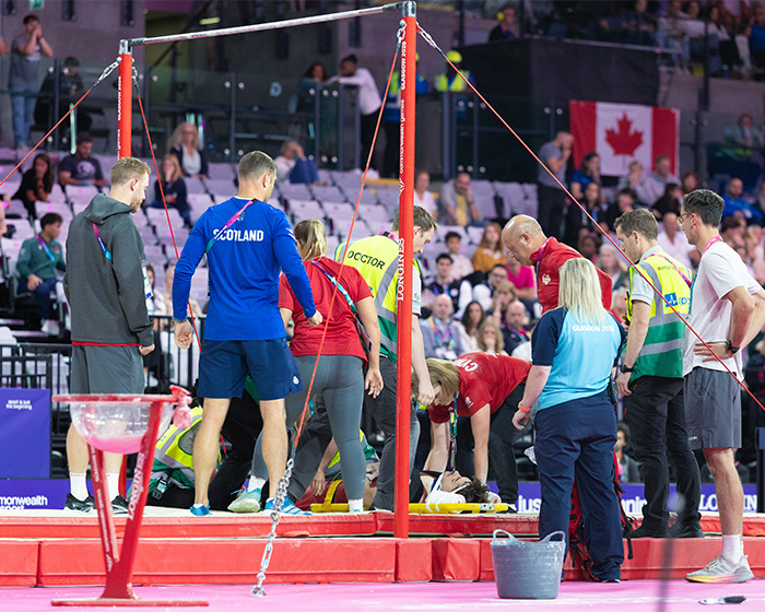 English gymnast being rushed to hospital after a horrific fall during the Commonwealth Games, surrounded by medical personnel.
