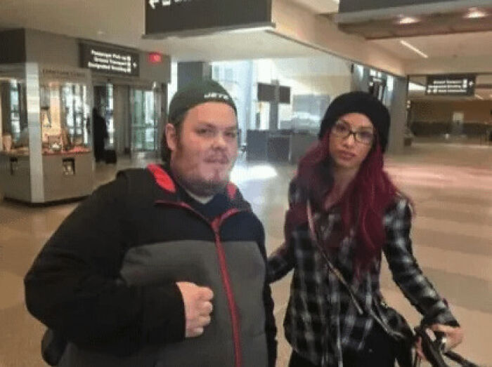 A celebrity, Sasha Banks, looks uncomfortable as a fan stands close for a photo in an airport.