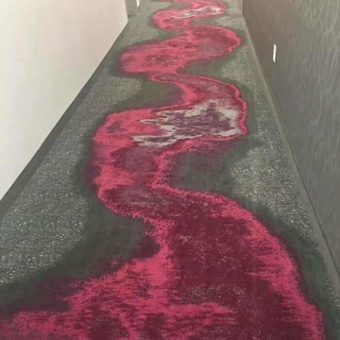 A hallway carpet with a wavy red and gray pattern that looks like a bloodstain, a design failure.