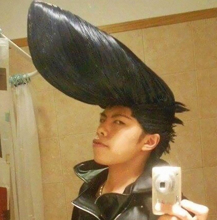 A young man with an extreme, gravity-defying pompadour hairstyle taking a selfie in a bathroom. This is one of many bad hair mistakes.