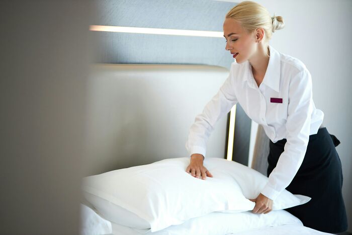 A hotel staff member making a bed, arranging pillows. Essential hotel industry secrets for a great vacation.