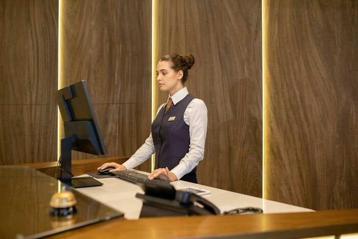 A hotel receptionist works at the front desk, sharing hotel industry secrets for your next vacation.