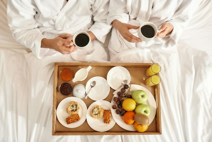 Two people in robes enjoying breakfast in bed, a helpful hotel industry secret for a comfortable vacation.