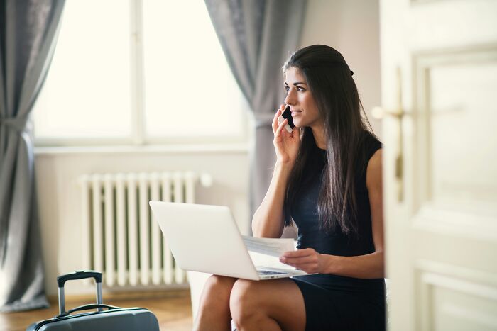 Woman in a hotel room with a laptop and phone, ready for vacation with helpful hotel industry secrets.