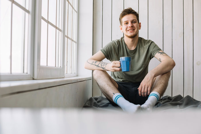 A young man smiling while holding a cup, trusting a house sitter with his home.